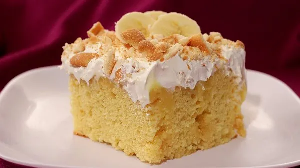 Slice of banana pudding poke cake topped with whipped topping and crushed Nilla wafers.