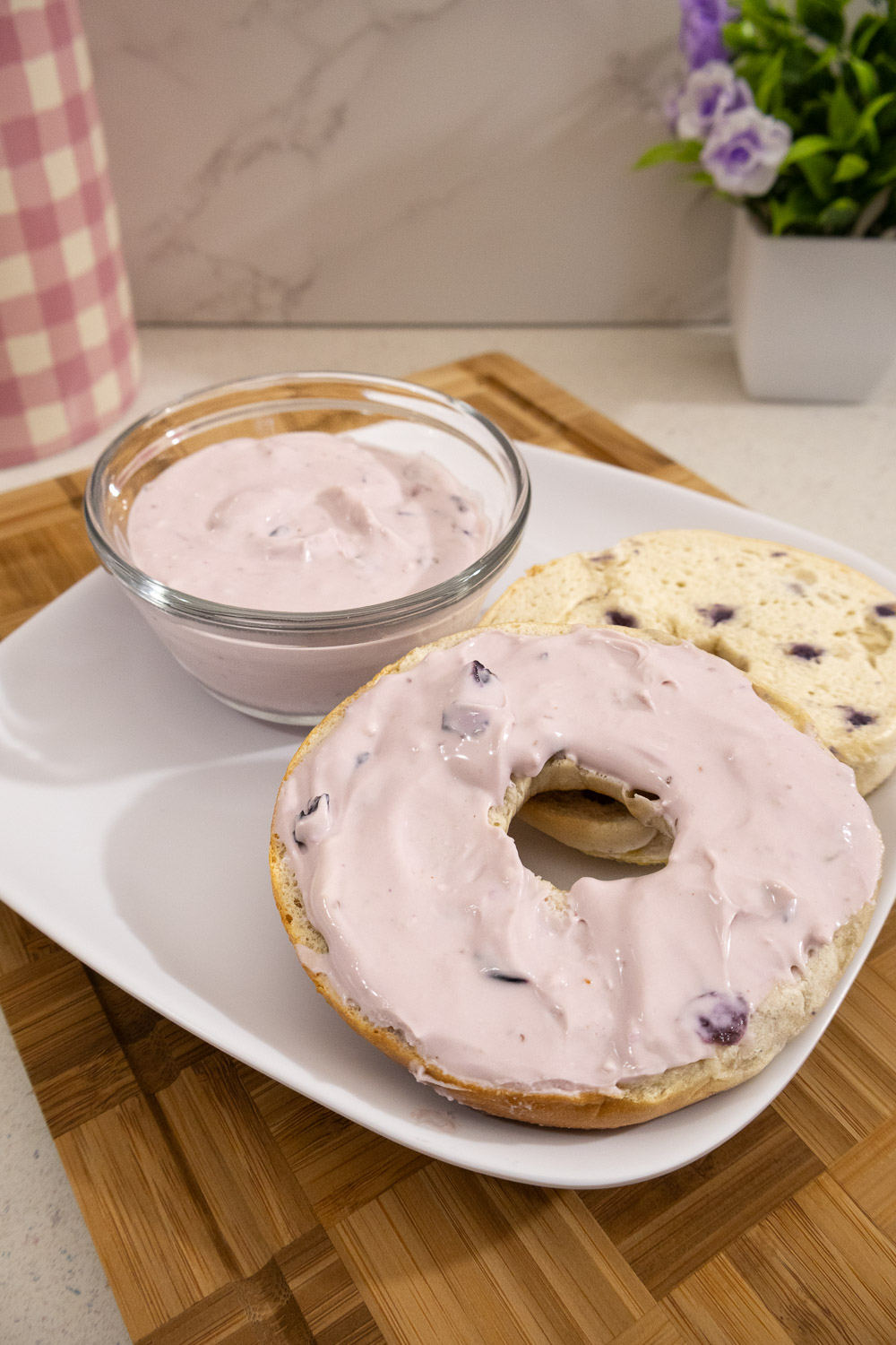 Homemade blueberry cream cheese spread on a blueberry bagel with a bowl of spread