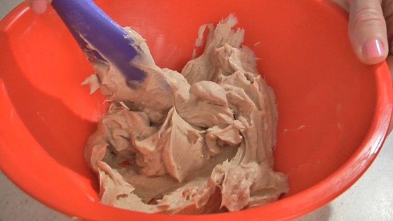 Close-up of a red, medium mixing bowl with cream cheese, sugar and cinnamon stirred together.