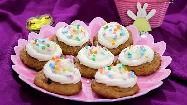 Plate of carrot cake cookies with cream cheese frosting surrounded by Easter decorations.