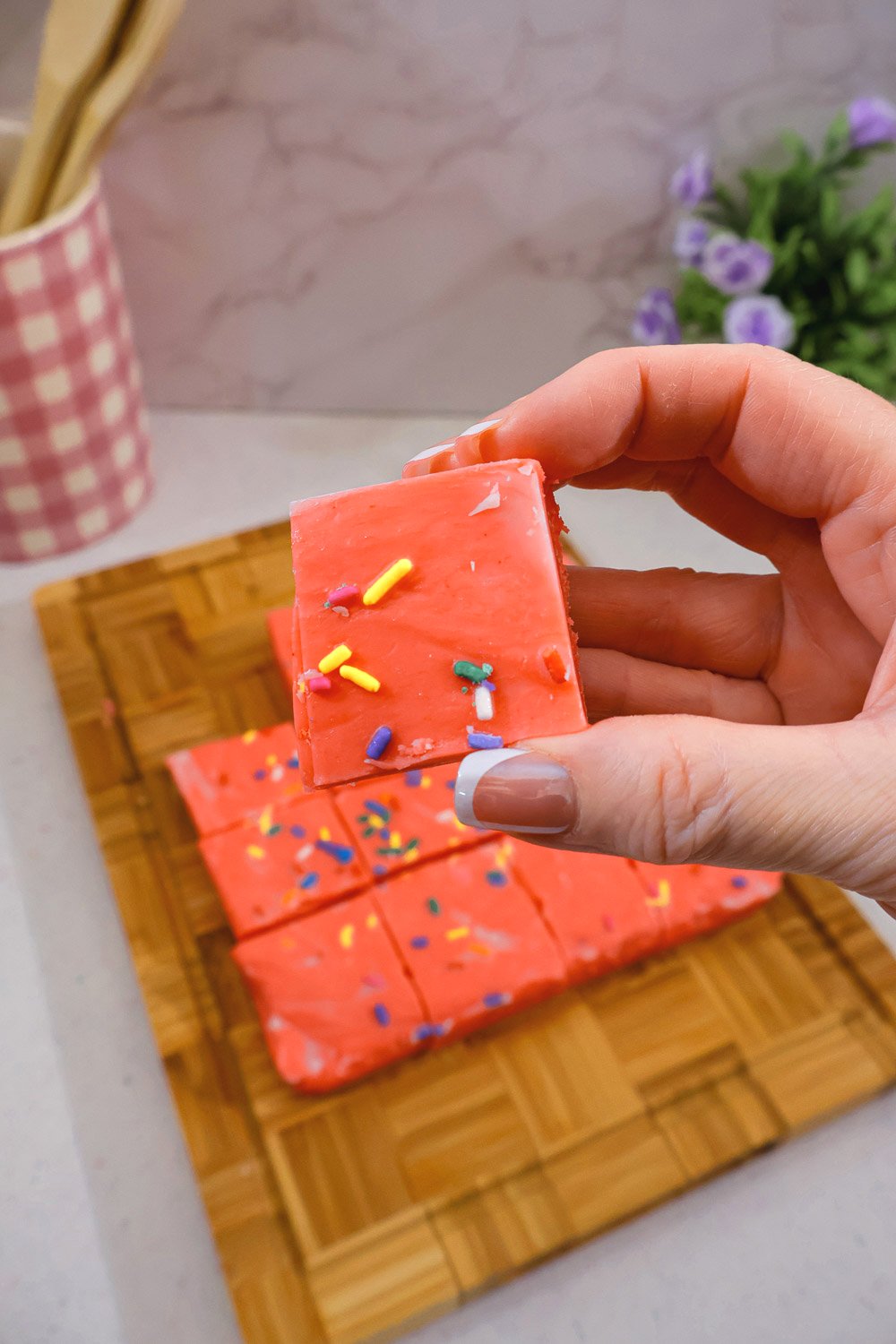 Hand holding a square of Cherry Kool-Aid fudge topped with colorful sprinkles