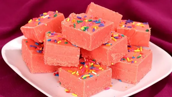 Stack of pretty, pink cherry Kool-Aid Fudge topped with colorful sprinkles on a white plate.