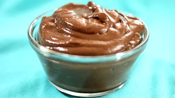 Clear bowl filled with chocolate avocado pudding against an aqua background.