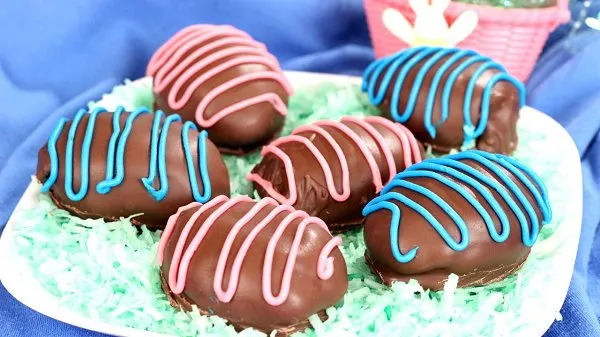 Chocolate peanut butter Easter eggs on a bed of green tinted flaked coconut with Easter decor in the background.