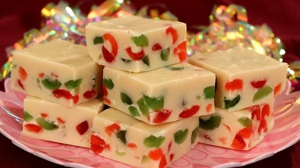Creamy white fudge loaded with festive red and green candied cherries stacked on a pink plate with a sparkly ribbon.