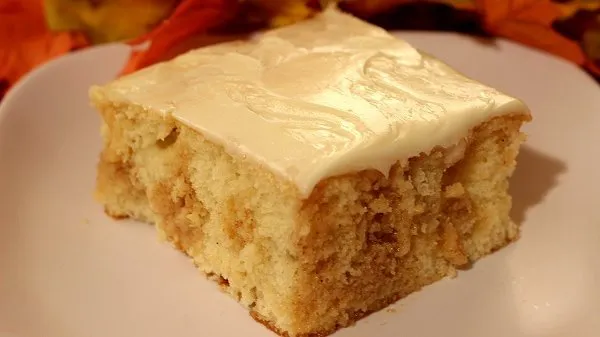 Slice of cinnamon roll poke cake on a white plate.