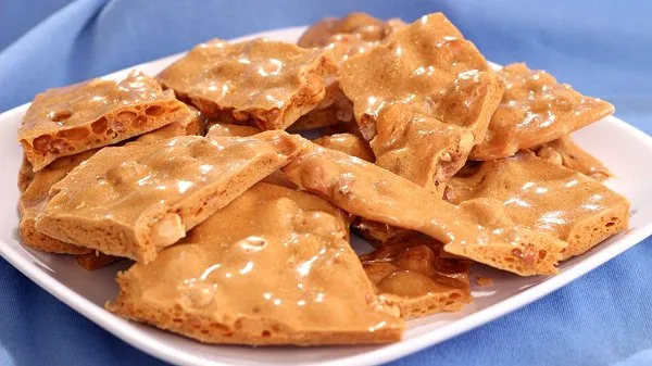 Crunchy peanut brittle piled on a white plate.
