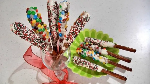 Colorful double dipped pretzel rods, in a glass and on a green plate, covered in candy and sprinkles
