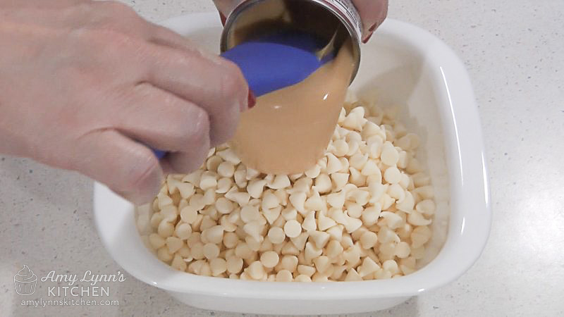A microwave-safe bowl with white chocolate chips and sweetened condensed milk.