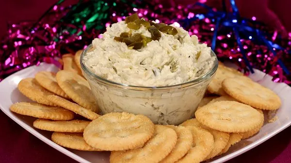 Clear bowl filled with easy jalapeno artichoke dip with extra slices of jalapenos on top.  Dip is surrounded by Ritz Crackers.