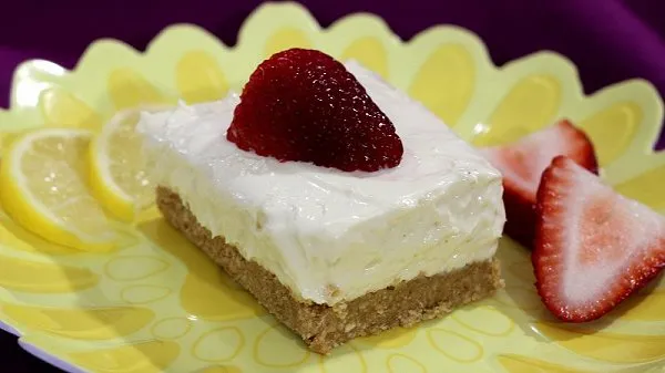 Slice of easy no-bake lemon cheesecake square topped with a strawberry.