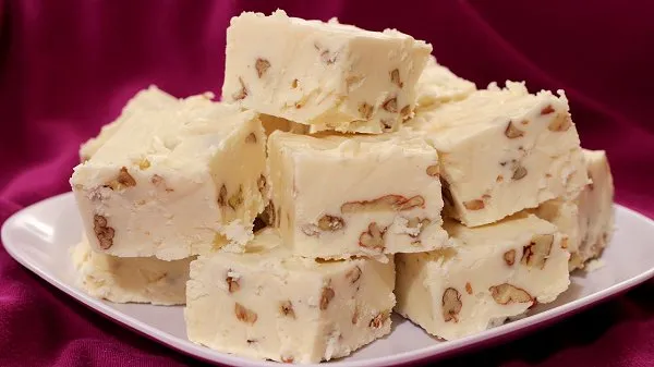 Stacked squares of homemade eggnog fudge with pecans on a white plate.