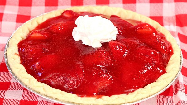 Fresh strawberry pie with glossy strawberry gelatin and halved strawberries layered in a golden baked crust. A chilled, fruit-forward dessert topped optionally with whipped cream.