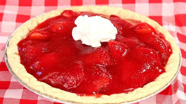 A whole, fresh strawberry pie topped with whipped cream.