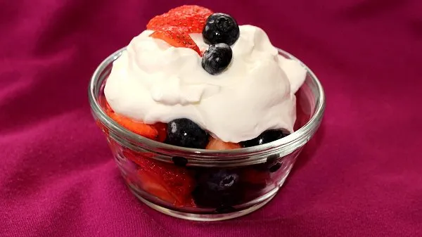 Bowl of fresh strawberries and blueberries topped with creamy Greek yogurt whipped cream.