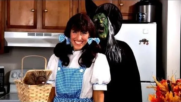 Amy Lynn dressed as Dorothy from The Wizard of Oz standing beside Frankie dressed as the Wicked Witch of the West, with a stuffed Toto doll in a basket on the counter.