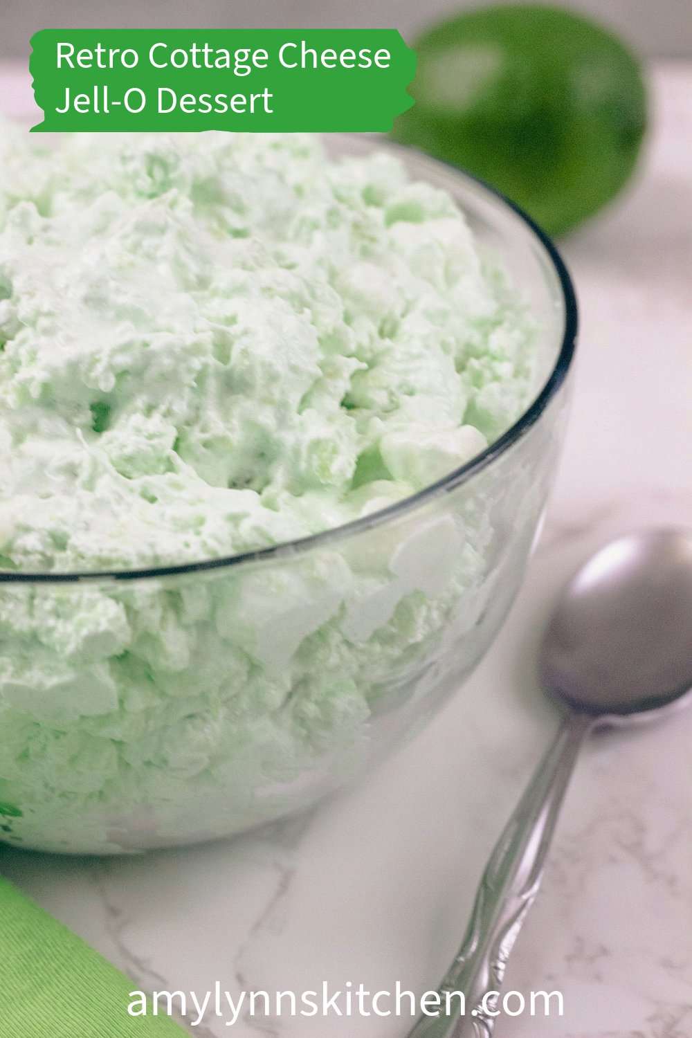 Bowl of lime Jell-O cottage cheese salad with pineapple and marshmallows surrounded by a spoon and fresh lime.