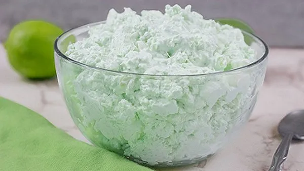 Bowl of lime cottage cheese fluff surrounded by limes and a spoon.