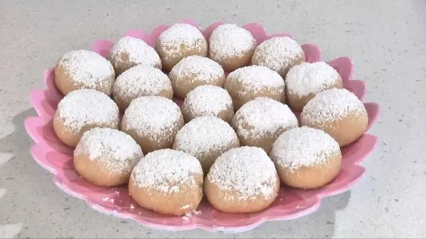 Melting snowball cookies topped with powdered sugar on a pink plate.