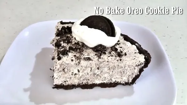 A slice of no bake oreo cookie pie topped with whipped cream and an Oreo Cookie on a white plate.