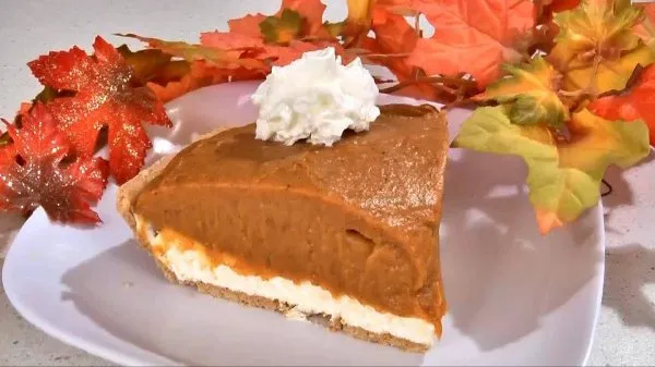 A slice of no bake pumpkin pie topped with whipped cream on a white plate surrounded by fall leaves decoration.