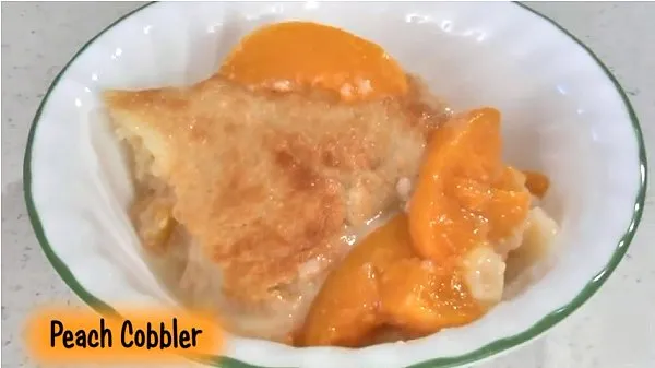 Peach cobbler surrounded by extra sliced peaches in a white bowl.