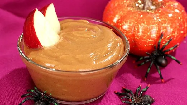 Bowl of peanut butter apple dip with two slices of apples and surrounded by Halloween decor.