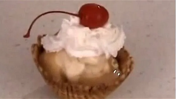Vanilla ice cream in a waffle cone bowl topped with peanut butter sundae sauce, whipped cream and a cherry.