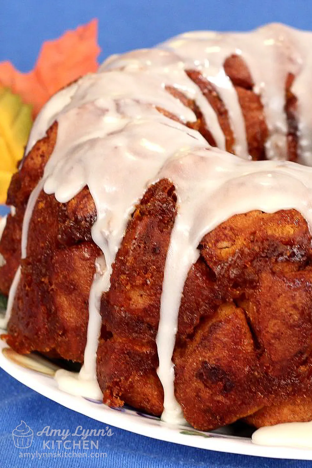 Pumpkin Cinnamon Roll Monkey Bread with icing drizzle on a plate with fall leaves in the background.