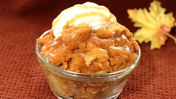 Pumpkin bread pudding, piled high in a clear bowl, topped with vanilla ice cream and caramel syrup.