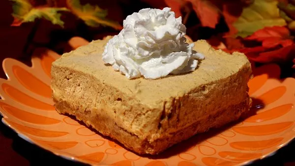 Slice of pumpkin delight topped with whipped cream served on an orange plate.