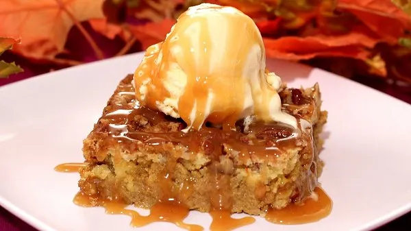 A slice of pumpkin dump cake, topped with vanilla ice cream and drizzled with caramel sauce, served on a white plate.