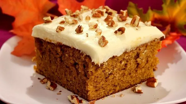Slice of pumpkin spice cake topped with cream cheese frosting and chopped pecans.