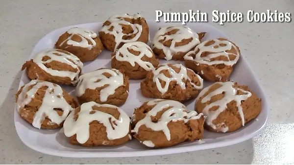 Pumpkin spice cookies drizzled with cream cheese frosting on a white plate.