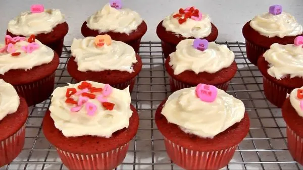  Rows of red velvet cupcakes topped with cream cheese frosting and candy.
