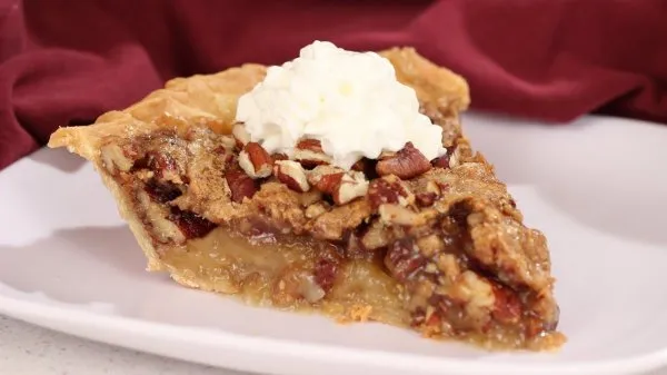 A slice of toffee pecan pie topped with whipped cream on a white plate.