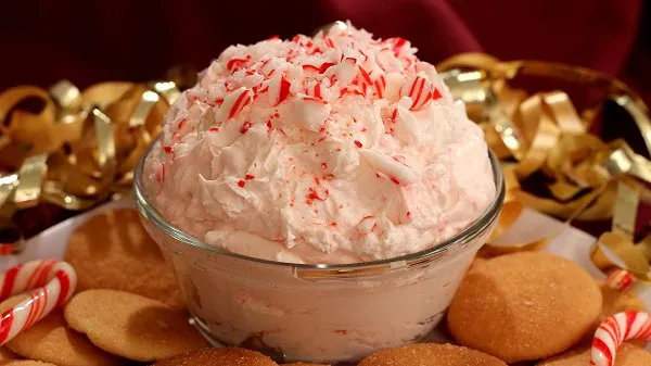Bowl of white chocolate peppermint dip topped with crushed candy canes surrounded by Nilla wafers and gold curly bows.