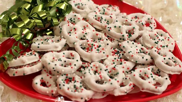 Pretzels dipped in white chocolate and covered in sprinkles on a red heart plate.